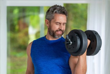 Dambılla egzersiz yapan bir adam. Erkek atlet dambılı kaldırıyor. Güçlü adam spor egzersizi yapar. Jimnastik. Dambılı bir sporcu. Sağlıklı bir yaşam tarzı. Kas gücü. Yanal yükseltme.