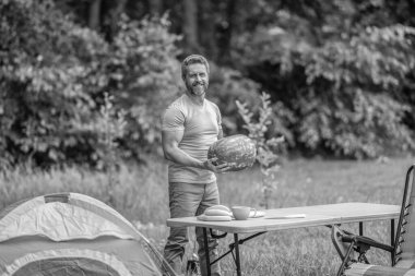 Kamp ve doğa pikniği. Adam kampı. Karpuz kampı pikniği. Lezzetli sağlıklı yiyecekler. Kampta taze yiyecek. Yaz kampında elinde karpuz tutan adam. Yaz günü erkek yürüyüşçüsü. Meyve yiyin..