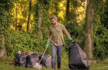 Çevreci adam. Çevresel koruma. Çevreyi koru. Çevre plastik kirliliği. Gönüllü adam ormanda çöp topluyor. Çevresel koruma. Atık azaltma stratejisi.