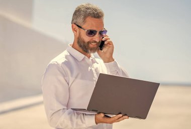 Başarılı iş adamı çevrimiçi olarak serbest çalışıyor. İnternette çalışan İspanyol iş adamı. Uzaktan kumanda çalışıyor. Telefon görüşmesi. İş adamı dışarıda dizüstü bilgisayarla çalışıyor. Adamın iş görüşmesi var..