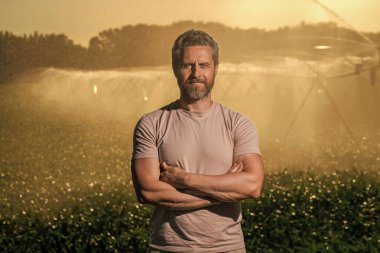 Sulama sisteminde tarımı sulayan bir adam. Kırsal kesimde bir çiftçi. Su püskürtme sulama tarlası. Damlatma sulama sistemi. Ekin sulama. Tarım ve tarım. Su süreci.