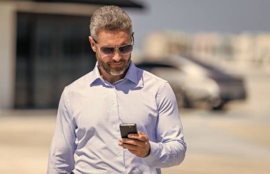 Akıllı telefon kullanan bir iş adamı. İnternette yakışıklı bir iş adamı sohbeti. İş adamı yürüyor. Şirket işi. Dışarıdaki telefonda iş adamı sohbeti. İş adamı telefonda sohbet ediyor. İş anlaşması.