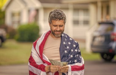 Amerika 'da vergi ödemek. Katma değer vergisi. Vergi sistemi. Vatansever adam para sayıyor. Amerikan bayrağı ve dolar parası olan adam. Enflasyon konsepti. Amerikan vergi politikası. İspanyol ve Amerikan bayrağı.