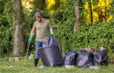 Gezegen kirliliği çevresel koruma. Ormanı temizliyorum. Çöp torbasına çöp koymak, çevre koruması. Gönüllü, çöpleri toplamaya yardım eder. Kirli orman. Çöp reklamı..