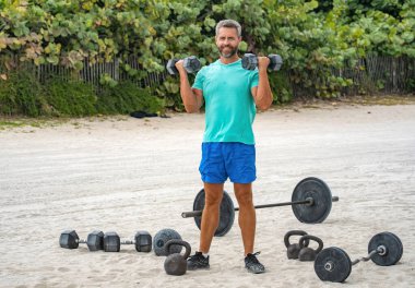 Güçlü adam spor egzersizi yapar. Jimnastik. Dambılı bir sporcu. Sağlıklı bir yaşam tarzı. Kas gücü. Güçlü trisepsler. Dambılla egzersiz yapan bir adam. Dambıl kaldıran sporcu, boşluğu kopyala.