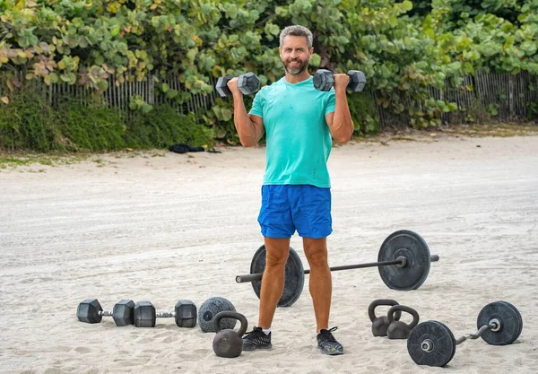 Güçlü adam spor egzersizi yapar. Jimnastik. Dambılı bir sporcu. Sağlıklı bir yaşam tarzı. Kas gücü. Güçlü trisepsler. Dambılla egzersiz yapan bir adam. Dambıl kaldıran sporcu, boşluğu kopyala.