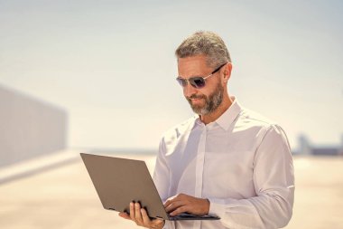 İnternette çalışan bir iş adamı. Uzaktan kumanda çalışıyor. Video konferansı. Dışarıda dizüstü bilgisayarda çalışan bir iş adamı. Adamın iş görüşmeleri var. Başarılı iş adamı çevrimiçi olarak serbest çalışıyor. İnternette toplantı.