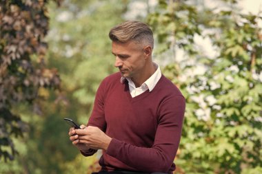 İş adamı dışarıdaki telefonu kullanır. Oturan olgun bir iş adamı. Sonbahar tarzı. Sonbahar parkındaki iş adamı. Kafkasyalı bir adamın günlük bir tarzı vardır. Olgun adam cep telefonu kullanır. Sabit iletişim.