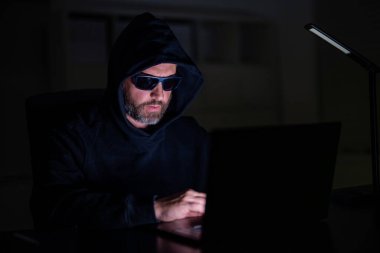 Hacker saldırısı. Geceleri ofiste bilgisayar korsanı. Siber saldırı. Siber suçlu ve çalıntı kişisel veriler. Dijital hırsız. Ofis laptopunda kapüşonlu bilgisayar programcısı, oyun. Güvenlik duvarı baypası.