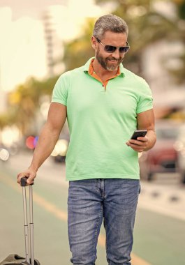 Gezgin telefon kullanıyor. Turist tatili rezervasyonu. Yaz gezisi için seyahat valizi. Yaz gezisini ayarlayan adam. İspanyol turist gezginleri kitabı internette. Seyahat çantalı bir turist..