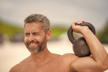 Güçlü, mutlu adam spor egzersizi yapar. Jimnastik. Sporcu adam kettlebell 'i tutuyor. Ağırlık kaldırma, ağırlık kaldırma antrenmanı. Olgun bir adam dışarıda kettlebell egzersizi yapıyor. Çaydanlık çanı kaldıran bir sporcu.