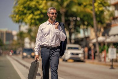 Başarılı bir iş adamı dışarıda evrak çantasıyla dolaşıyor. İş adamı evrak çantasını tutar. İşadamı başarılı bir anlaşma yaptı. Şirket işi. Takım elbiseli zengin iş adamı. İş portresi. Liderlik pozisyonu.