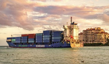 Miami, Florida, ABD - 14 Aralık 2024: Kargo Kıyısı mavi gemi hizmetleri konteynır, hava günbatımı manzaralı. Kargo gemisinde nakliye konteynırı. Kargo gemisi. Miami limanı. Konteyner gemisi.