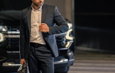 Takım elbiseli zengin iş adamı. İş portresi. Çantası park yerinde, manzarası kesik başarılı bir iş adamı. İş adamı evrak çantasını tutar. Takım elbiseli olgun iş adamı. Şirket işi. Boşluğu kopyala.