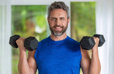 Güçlü adam spor egzersizi yapar. Jimnastik. Dambılı bir sporcu. Sağlıklı bir yaşam tarzı. Kas gücü. Güçlü trisepsler. Dambılla egzersiz yapan bir adam. Erkek atlet dambılı kaldırıyor.