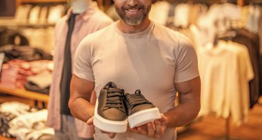 Ayakkabı seçen olgun bir adam. Spor ayakkabıları. Lüks mağazada spor ayakkabıları. Ayakkabı mağazası. Erkek ayakkabısı mağazası. Erkek alışverişi, spor ayakkabılar. Kumaş butikte şık bir adam. Sunulan boyut.