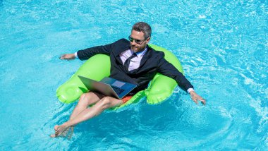 Uzaktan kumanda çalışıyor. Yaz tatili. Komik çılgın iş adamı resmi olarak havuzda dinleniyor. Çılgın yaz. Eğlenceli iş hayatı. Yüzme havuzunda dizüstü bilgisayarı olan iş adamı..