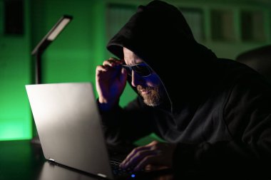 Siber suçlular ve çalınan finansal veriler. Dijital para hırsızı. Ofis laptopunda kapüşonlu bilgisayar programcısı, oyun. Hacker saldırısı. Geceleri ofiste bilgisayar korsanı. Siber saldırı. Gece hackerı.
