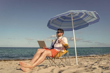 Bilgisayarı olan uzaktan kumandalı bir iş adamı. Kumsalda dizüstü bilgisayar kullanan bir iş adamı. Seyahat ve iş. Sea Beach 'te serbest çalışan bir adam. Yaz tatilindeki iş adamı. Çevrimiçi serbest platform.