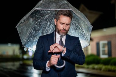 İş adamı caddede nöbet tutuyor. İş adamı kontrol zamanı. Geç ve dakik. Dakik bir iş adamı. Yağmurlu havada bekleyen bir adam. İş adamı şemsiyeyle yağmurun altında bekler. Zaman yönetimi.