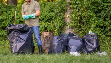 Ormanı temizliyorum. Çöp torbasına çöp koymak, çevre koruması. Gönüllü çöp toplamaya yardım eder. Kirli orman. Çöp yığını. Gezegen kirliliği çevre koruma, kırpılmış görüş.