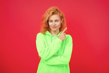 Kızıl saçlı manken kapüşonlu ve kot pantolon giyiyor. Kapüşonlu kadın koşucu. Pembe üzerine izole edilmiş kız kazağı. Kapüşonlu havalı bir kadın. Şık, sıradan tarzda şık bir kız. Reklamlara işaret ediyor..