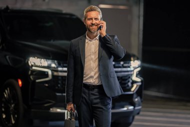 Telefon görüşmesi. İş portresi. Çantası park yerinde başarılı bir iş adamı. İş adamı evrak çantasını tutar. Takım elbiseli olgun iş adamı. Şirket işi. Takım elbiseli zengin iş adamı.