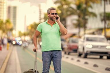 Turist tatili rezervasyonu. Yaz gezisi için seyahat valizi. Yaz gezisini ayarlayan adam. İspanyol turist seyahat kitabı internette. Seyahat çantalı bir turist. Gezgin telefon kullanıyor. Seyahat yaşam tarzı.