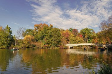 New York City, ABD - 25 Ekim 2023: Sonbahar ağaçlı Central Park. Sonbahar doğası. Gölde teknesi olan New York City Central Park. Sonbahar manzarası. Central Park 'ta insanlar kürek çekiyor..