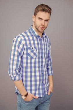 Sıradan tişörtlü bir adamın portresi. Tıraşsız adamın zarif portresi. Gri yolda izole edilmiş bir adam. Kareli gömlek giyen milenyum adamı. Milenyum erkeğinin gündelik tarzı. Temel gardırop.