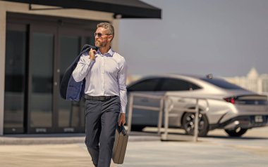 İş adamı evrak çantasını tutar. Başarılı bir anlaşmadan sonra bir iş adamı. Şirket işi. Takım elbiseli zengin iş adamı. İş portresi. Başarılı bir iş adamı evrak çantasıyla dışarıda dolaşıyor, boşluğu kopyala.