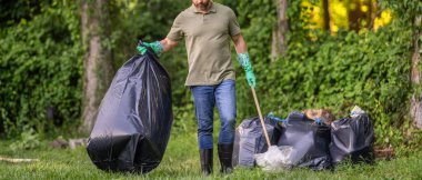 Çöp torbasına çöp koymak, çevre koruması. Gönüllü çöp toplamaya yardım eder. Kirli orman. Çöp yığını. Gezegen kirliliği çevresel koruma. Ormanı temizliyor, manzarayı kesiyor..