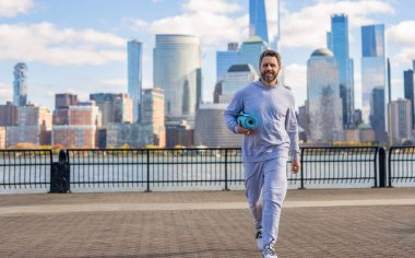 Manhattan 'da spor kıyafetli bir adam. Vücuduna uygun. Yoga koçu. Sporcu adam antrenmana hazır. Sağlıklı bir yaşam tarzı. Spor ve spor. Eğitim için yoga minderi. New York 'ta sporcu, afiş.