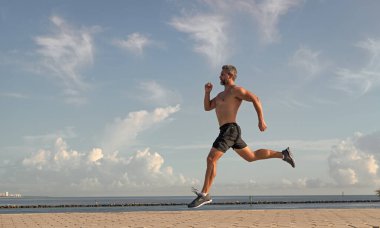 Spor koşucusu egzersiz yapar. Spor yaşam tarzı ve sabah koşusu. Koşucu çıplak gövde koşuyor. Spor ve sağlık. Kumsalda koşan adam. Sağlıklı bir yaşam tarzı. Yazın koşan sporcu, afiş.