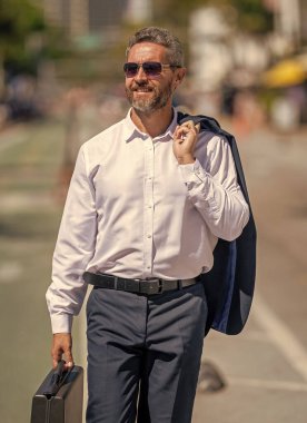 Takım elbiseli zengin iş adamı. İş portresi. Başarılı bir iş adamı dışarıda evrak çantasıyla dolaşıyor. İş adamı evrak çantasını tutar. Başarılı bir anlaşmadan sonra bir iş adamı. Şirket işi. Liderlik.