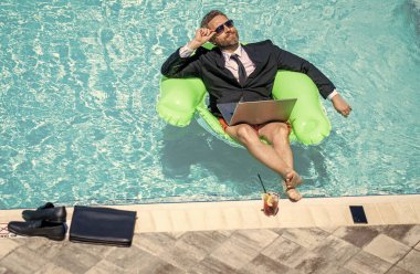 Çevrimiçi çalışan serbest çalışan. Adam havuzda serbest çalışmak için dizüstü bilgisayar kullanıyor. Serbest iş yapma. Yaz tatilindeki iş adamı. İş adamı görüntülü konuşma yapıyor. Serbest çalışan adamın çevrimiçi video görüşmesi var..