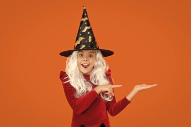 Mutlu Cadılar Bayramı. Cadılar Bayramı kostümlü cadı kız turuncu üzerine izole edilmiş. Cadılar Bayramı indirimi. İşaret parmağı. Tüm Cadılar Bayramı reklamları. 31 Ekim. Cadı kostümlü kız. Ürünü sunuyorum..