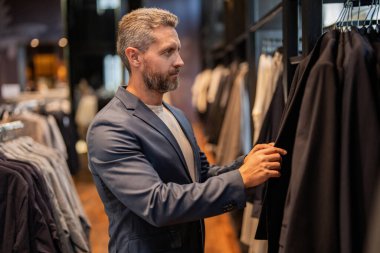 Butikte alışveriş yaparken klasik terzilik kıyafeti giyen adam. Başarılı iş adamları için klasik takım elbise. Takım elbiseli moda mağazası. İş adamı resmi etkinlik için takım elbiseyi seçti. Seçim yapmak.