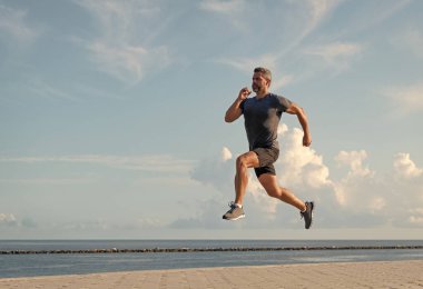 Yazın koşan sporcu. Spor koşuculuğu eğitimi. Sağlıklı yaşam tarzı ve günlük koşular. Koşan koşucu. Spor ve spor. Kumsalda koşan adam. Spor yaşam tarzı. Boşluk afişini kopyala.