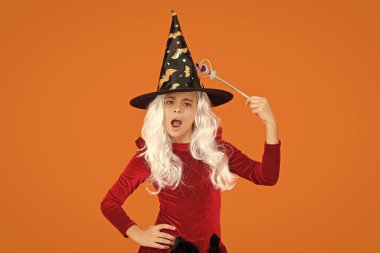 Cadılar Bayramı kostümlü partisi. Tüm Cadılar Bayramı cadıları. Cadı kostümlü kız sihirli değneği tutuyor. Mutlu Cadılar Bayramı. Cadılar Bayramı kostümlü cadı kız turuncu üzerine izole edilmiş. Şeker mi şaka mı? Eğleniyorum..