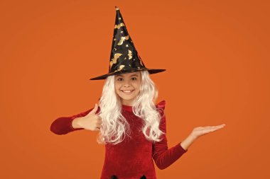 Tüm Cadılar Bayramı reklamları. 31 Ekim. Cadı kostümlü kız. Ürünü sunuyorum. Mutlu Cadılar Bayramı. Cadılar Bayramı kostümlü cadı kız turuncu üzerine izole edilmiş. Cadılar Bayramı indirimi. Başparmak yukarı..