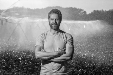 Sulama sisteminde tarımı sulayan bir adam. Kırsal kesimde bir çiftçi. Su püskürtme sulama tarlası. Damlatma sulama sistemi. Ekin sulama. Tarım ve tarım. Su süreci.