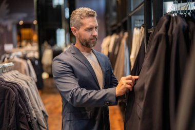 Mağaza müdürü şık bir takım seçmiş. Butikte alışveriş yaparken klasik terzilik kıyafeti giyen adam. Başarılı iş adamları için klasik takım elbise. Takım elbiseli moda mağazası. İş adamı etkinlik için ceket seçer.
