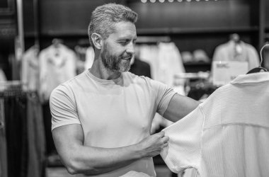 Tişört seçen olgun bir adam. Tasarımcı kıyafeti. Lüks mağazada günlük tarz erkek giyim. Şık bir adam için lüks butik alışverişi. Erkek giyim mağazası. Erkek giyim mağazasında şık bir adam. Kaliteli kumaş.