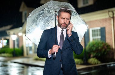 Şemsiye altında iş görüşmesi. İş adamı yağmurda dikilirken telefonda konuşur. Takım elbiseli bir iş adamı cep telefonuyla konuşuyor. Yağmurlu sokakta telefonu olan bir iş adamı. Yağmurda iş adamı.