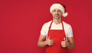 Kırmızı barmen önlüklü ve Noel Baba şapkalı mutlu bir olgun adam. başparmak yukarı.