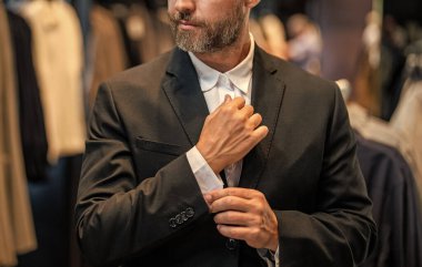 İspanyol iş adamı terzilik ve takım elbise seçiyor. Bespoke terziliği. Takım elbise mağazasında iyi giyimli erkek model. Perakende satış asistanı şık bir adamın takım elbise bulmasına yardımcı olur. İşadamı şık bir takım elbise seçmiş..