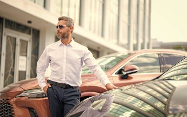 Zengin İspanyol iş adamı başarısını ifade ediyor. Lüks bir iş. Pahalı arabanın yanındaki zengin adam. Lüks iş seyahati. Klasik takım elbiseli, afiş giymiş kendine güvenen zengin iş adamı. Olgun iş adamı.