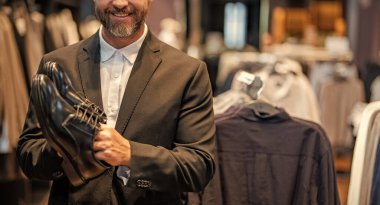 Ayakkabı mağazası. İş adamı dükkanda şık ayakkabılar seçer. Resmi görünmek için klasik deri ayakkabılar. Resmi ayakkabı. Deri ayakkabılar. Ayakkabı mağazasındaki tezgahtar adam klasik ayakkabı ve afiş tutuyor..