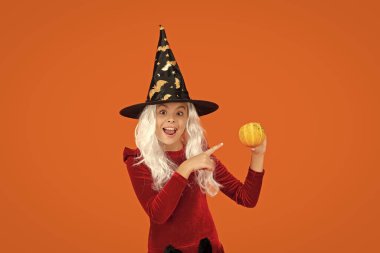 31 Ekim balkabağı. Kostüm partisi. Cadılar Bayramı balkabağı cadı kızın elinde. Cadılar Bayramı cadısı, turuncu üzerine izole edilmiş. Cadılar Bayramı 'nda balkabağı. Cadıların Cadılar Bayramı kostümü. İşaret parmağı.